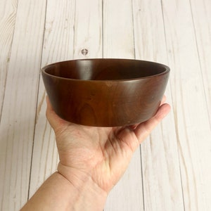 Indian Rosewood wooden bowl on woodgrain table - hand holding bowl to give idea of the size