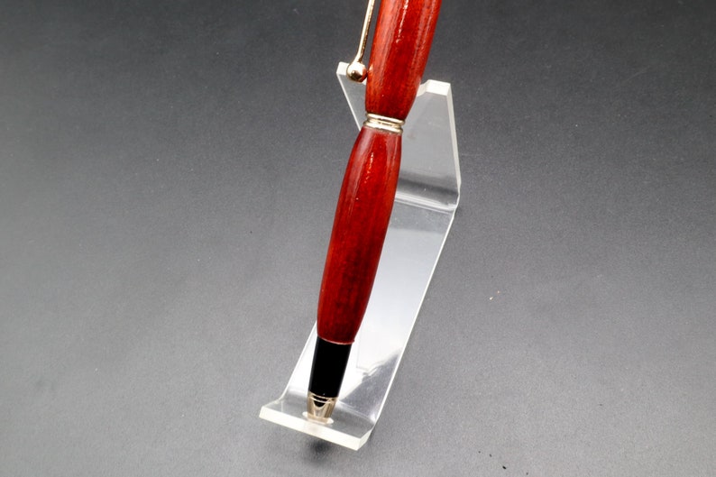 View of barrel for Bloodwood stylus pen with gold hardware on clear pen stand over black background