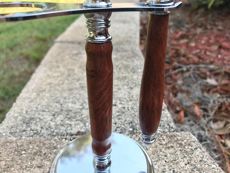 Close-up of eucalyptus shaving set with brush, stand, and razor handle sitting outside on a paver stone with grass in the background - focusing on the stand and the razor handle