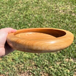 Shallow bowl made of Cypress wood being held in natural light - angled side view to see side and inside of bowl at the same time