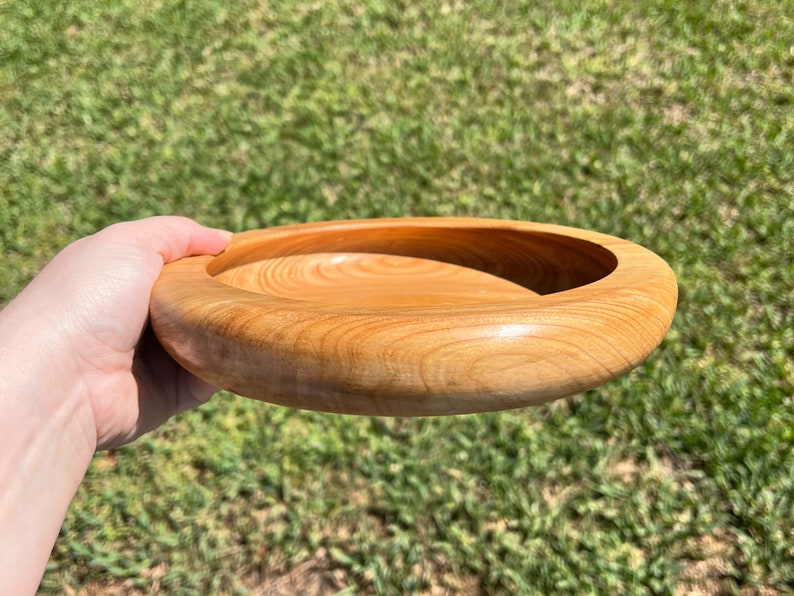 Shallow bowl made of Cypress wood being held in natural light - angled side view to see side and inside of bowl at the same time