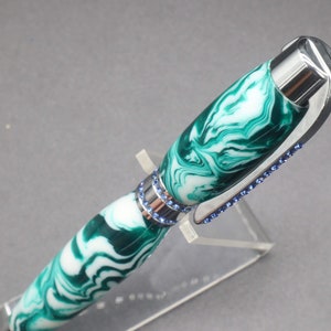 Close-up view of top of green and white (aka seafoam green) princess pen with blue crystals and chrome hardware on clear pen stand.