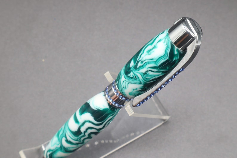 Close-up view of top of green and white (aka seafoam green) princess pen with blue crystals and chrome hardware on clear pen stand.