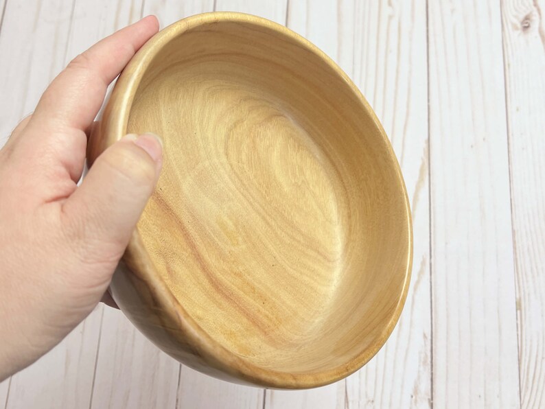 Shallow bowl made from camphor wood - being held at angle to show inside of bowl