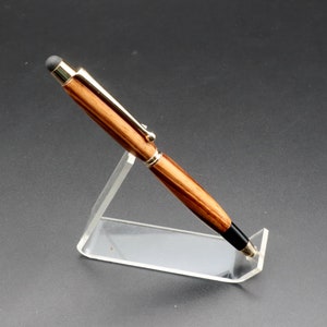 Side view of Zebrawood stylus pen with 24kt gold hardware in clear pen stand over black background