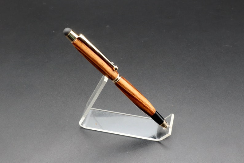 Side view of Zebrawood stylus pen with 24kt gold hardware in clear pen stand over black background