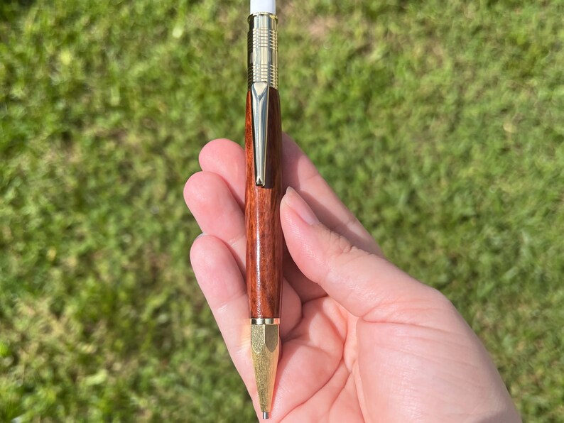 Holding the eucalyptus wood 2mm mechanical pencil in natural light to show off the reddish brown of the wood and the gold hardware.