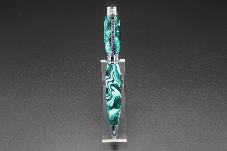 Front view of green and white (aka seafoam green) princess pen with blue crystals and chrome hardware on clear pen stand.