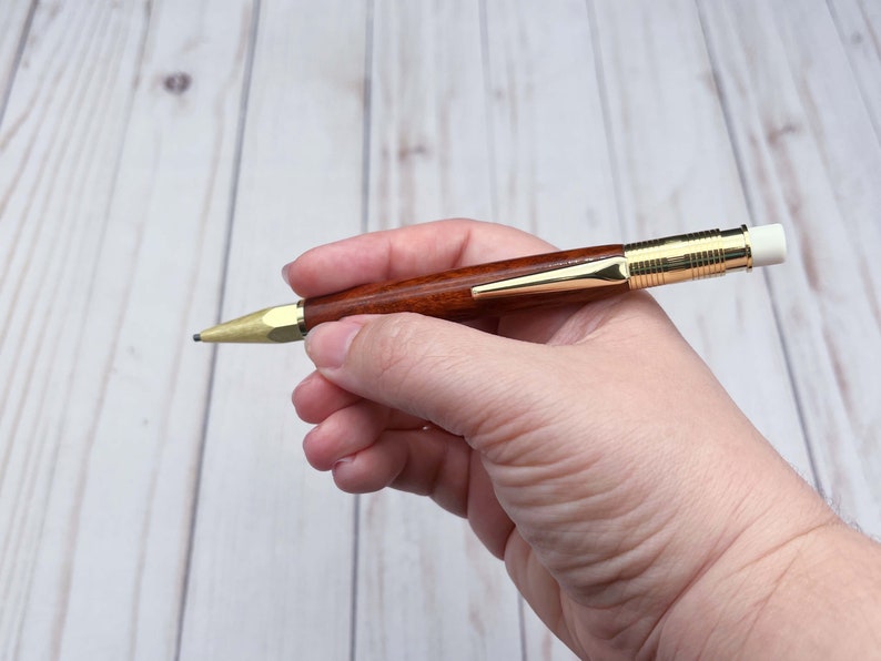 Holding the eucalyptus wood 2mm mechanical pencil under bright lights to show off the reddish brown of the wood and the gold hardware.