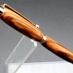 Close-up of wood for Zebrawood stylus pen with 24kt gold hardware in clear pen stand over black background