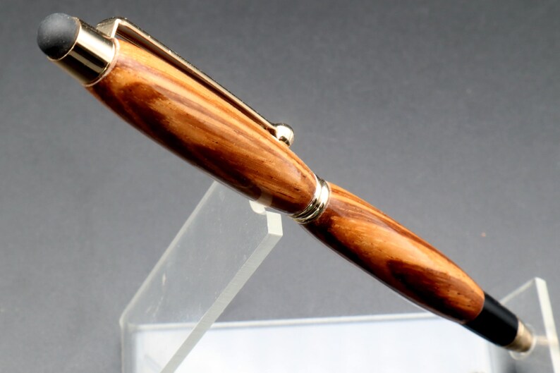 Close-up of wood for Zebrawood stylus pen with 24kt gold hardware in clear pen stand over black background