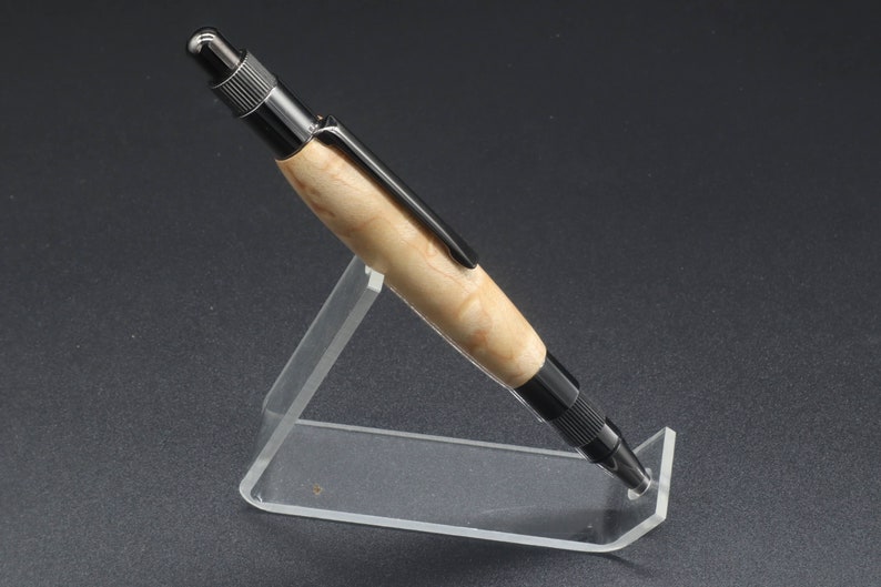 Full right side view of click pen made with birds eye maple wood and black hardware. It's in a clear pen stand on a dark background. Maple wood is a light, cream-colored wood with darker brown swirls in the grain.