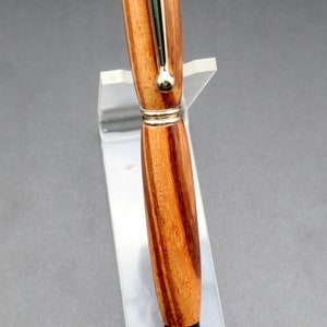 Close-up of wood and hardware for Zebrawood stylus pen with 24kt gold hardware in clear pen stand over black background