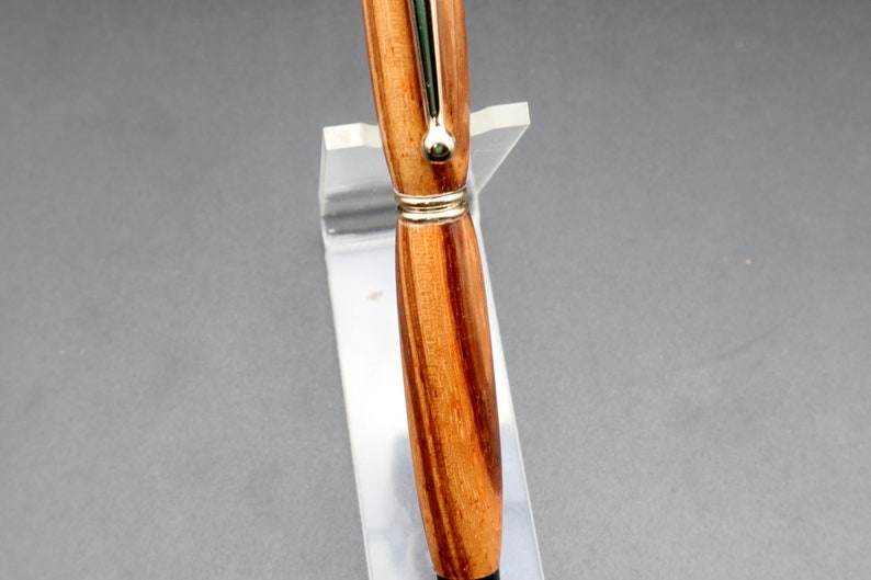 Close-up of wood and hardware for Zebrawood stylus pen with 24kt gold hardware in clear pen stand over black background