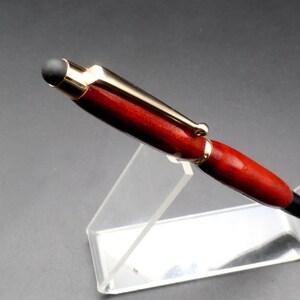 Top view of Bloodwood stylus pen with gold hardware on clear pen stand over black background