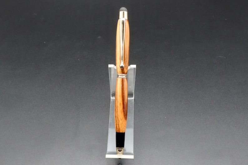 Front view of Zebrawood stylus pen with 24kt gold hardware in clear pen stand over black background