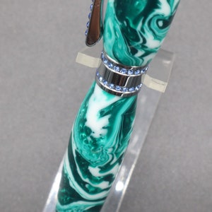 Close-up view of center of green and white (aka seafoam green) princess pen with blue crystals and chrome hardware on clear pen stand.