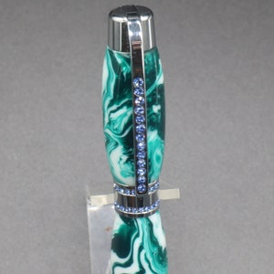 Close-up view of top of green and white (aka seafoam green) princess pen with blue crystals and chrome hardware on clear pen stand.