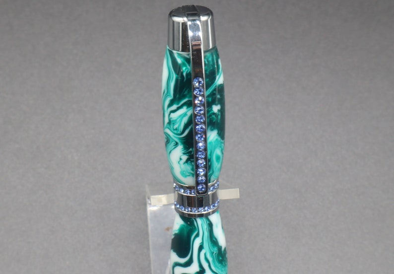 Close-up view of top of green and white (aka seafoam green) princess pen with blue crystals and chrome hardware on clear pen stand.