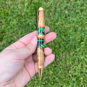 Holding olive wood and resin twist pen with satin gold hardware - in natural light