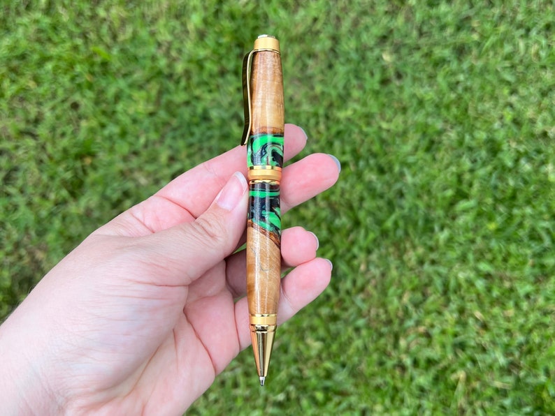 Holding olive wood and resin twist pen with satin gold hardware - in natural light