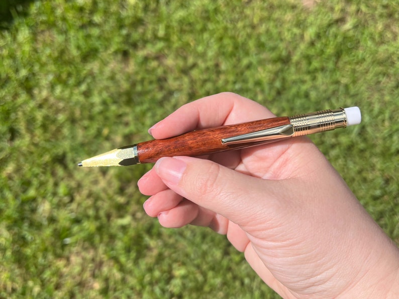 Holding the eucalyptus wood 2mm mechanical pencil in natural light to show off the reddish brown of the wood and the gold hardware.