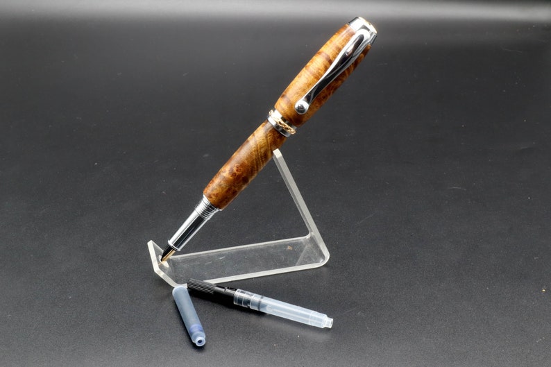 View of pen with cap off and ink refill for Fountain pen made with gold and black maple burl and chrome and gold hardware on clear pen stand over black background