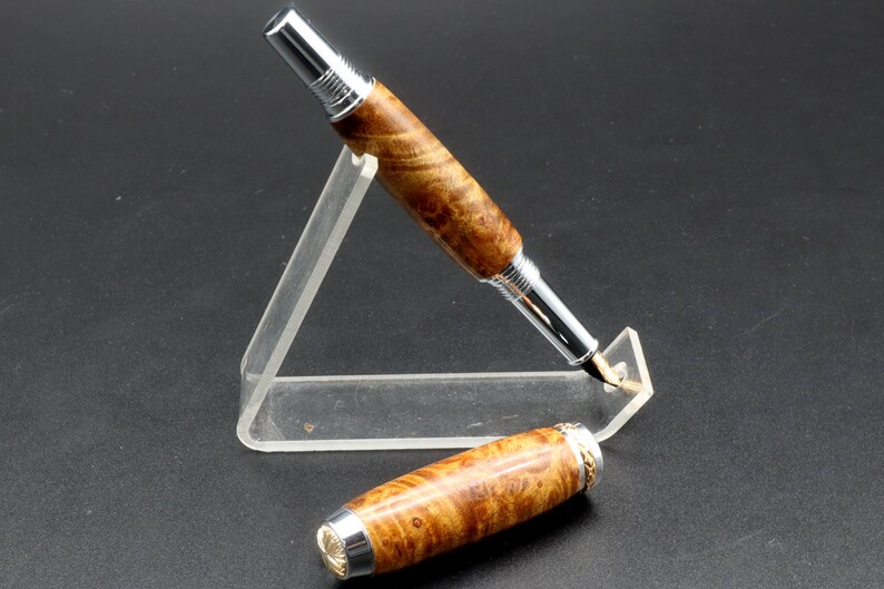 View of pen with cap off for Fountain pen made with gold and black maple burl and chrome and gold hardware on clear pen stand over black background