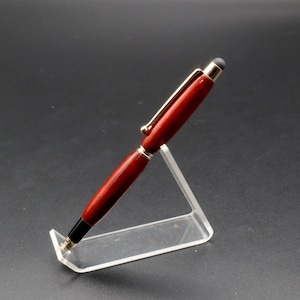 Side view of Bloodwood stylus pen with gold hardware on clear pen stand over black background