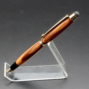 Side view of Zebrawood stylus pen with 24kt gold hardware in clear pen stand over black background