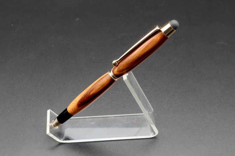 Side view of Zebrawood stylus pen with 24kt gold hardware in clear pen stand over black background