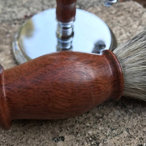 Close-up of eucalyptus shaving set with brush, stand, and razor handle sitting outside on a paver stone with grass in the background - focusing on the badger hair brush