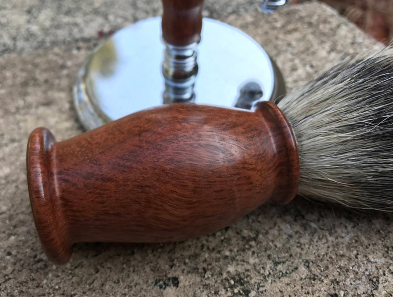 Close-up of eucalyptus shaving set with brush, stand, and razor handle sitting outside on a paver stone with grass in the background - focusing on the badger hair brush