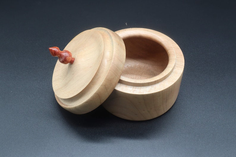 Wooden bowl made of maple and tulipwood with lid. Lid propped up against bowl.