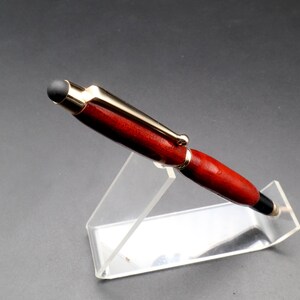 Top view of Bloodwood stylus pen with gold hardware on clear pen stand over black background