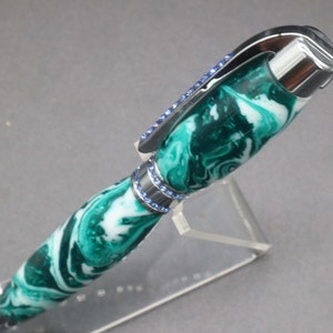 Close-up view of top of green and white (aka seafoam green) princess pen with blue crystals and chrome hardware on clear pen stand.