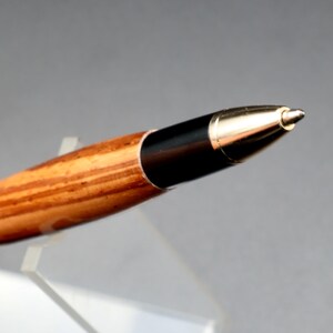 Close-up of pen tip for Zebrawood stylus pen with 24kt gold hardware in clear pen stand over black background