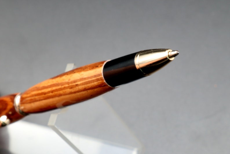 Close-up of pen tip for Zebrawood stylus pen with 24kt gold hardware in clear pen stand over black background