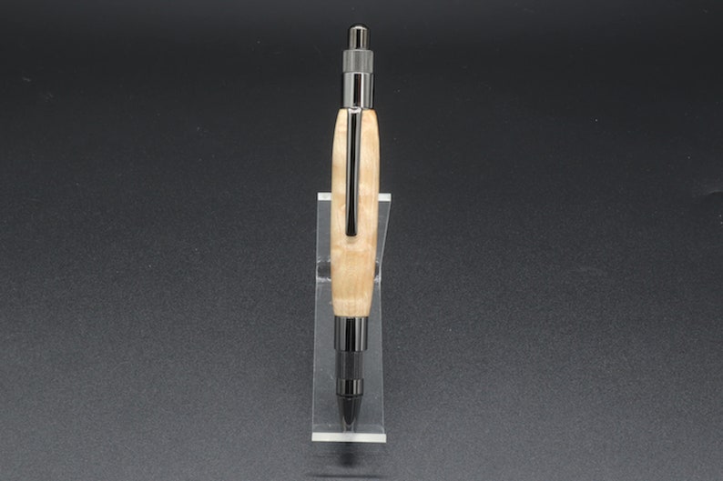Full front view of click pen made with birds eye maple wood and black hardware. It's in a clear pen stand on a dark background. Maple wood is a light, cream-colored wood with darker brown swirls in the grain.