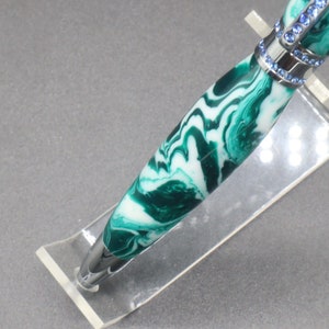 Close-up view of bottom/tip of green and white (aka seafoam green) princess pen with blue crystals and chrome hardware on clear pen stand.