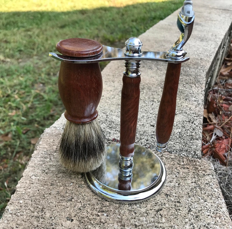 Eucalyptus shaving set with brush, stand, and razor handle sitting outside on a paver stone with grass in the background