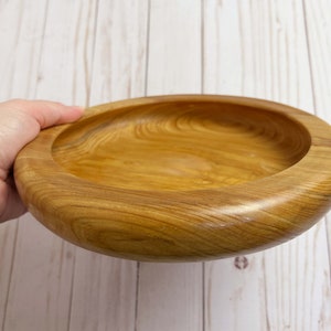 Shallow bowl made of Cypress wood being held - side view at an angle to see inside of bowl