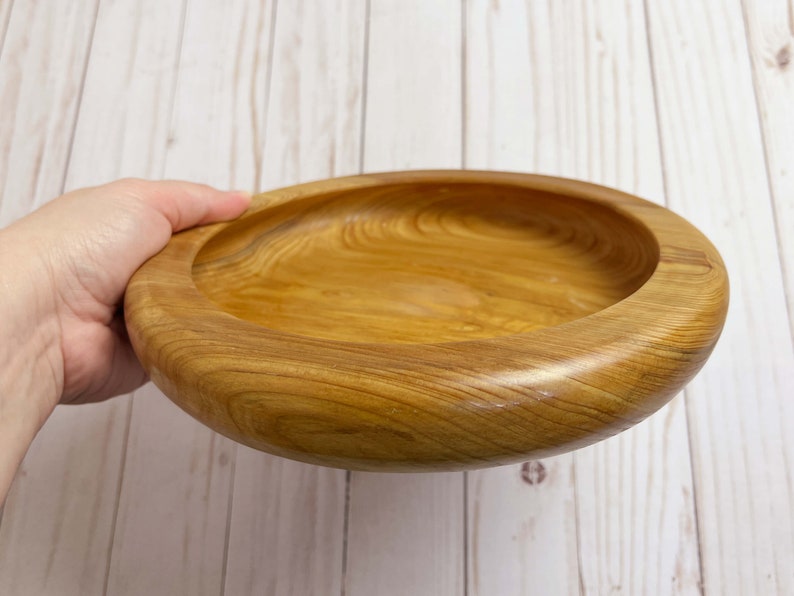 Shallow bowl made of Cypress wood being held - side view at an angle to see inside of bowl