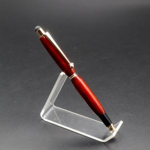 Side view of Bloodwood stylus pen with gold hardware on clear pen stand over black background