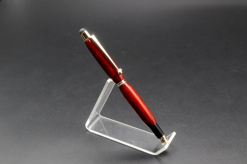 Side view of Bloodwood stylus pen with gold hardware on clear pen stand over black background