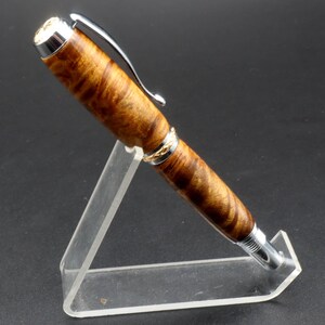 Side view of Fountain pen made with gold and black maple burl and chrome and gold hardware on clear pen stand over black background