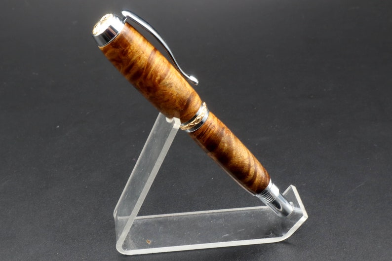 Side view of Fountain pen made with gold and black maple burl and chrome and gold hardware on clear pen stand over black background