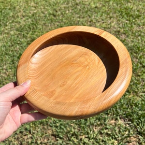 Shallow bowl made of Cypress wood - being held in natural light, angled view to see inside of bowl