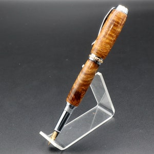 Side view of Fountain pen made with gold and black maple burl and chrome and gold hardware on clear pen stand over black background