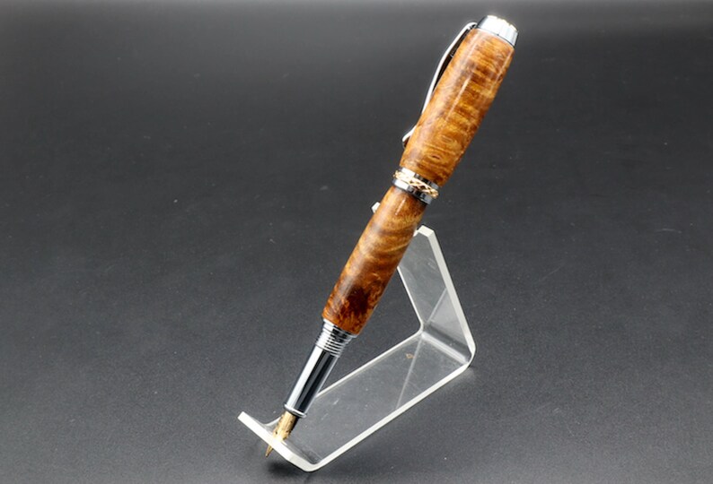 Side view of Fountain pen made with gold and black maple burl and chrome and gold hardware on clear pen stand over black background